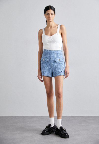 Top de bumbac alb tricotat cu cusături decorative asortat cu pantaloni scurți din tweed albastru, cu două buzunare și detalii cu nasturi aurii. Pantofi negri.
