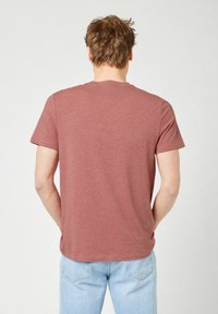 Korte mouwen, bordeauxrood t-shirt met een ronde hals; zachte textuur; gedragen met lichtblauwe jeans; zichtbare stiksels op de mouwen en de zoom.