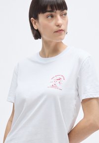 T-shirt en coton blanc à manches courtes, avec un motif de dessin animé rose et le texte "ONE MORE COFFEE, BEST ESPRESSO IN TOWN."