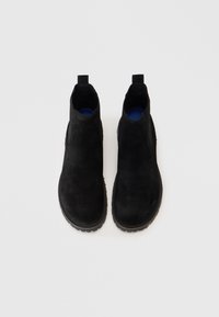 Un paio di stivali Chelsea in suede neri con pannelli elastici neri e suole blu visibili su uno sfondo bianco.