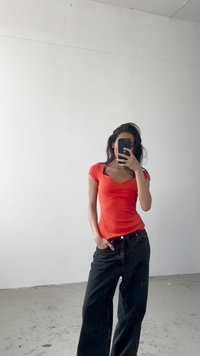 Red ribbed short-sleeve top with a v-neck, paired with loose black high-waisted jeans. The background is plain white, with minimal detail.