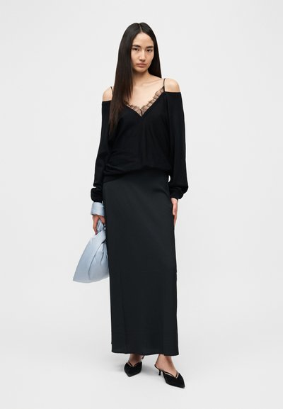 Jupe longue noire associée à un haut noir à épaules dénudées avec bordure en dentelle. Accessoires : un sac bleu clair et des chaussures noires à talons.