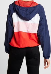 Czerwono-biało-granatowa kurtka z kapturem w kolorowym bloku z teksturowanym wykończeniem. Posiada siateczkowy kaptur i elastyczne mankiety, zaprojektowana z myślą o swobodnym kroju.