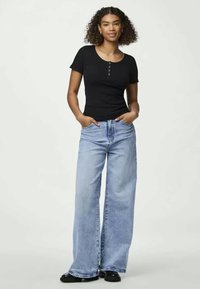 Camiseta henley preta de manga curta com três botões, combinada com calças de ganga largas de tom azul claro, apresentando um efeito desbotado e costuras visíveis.