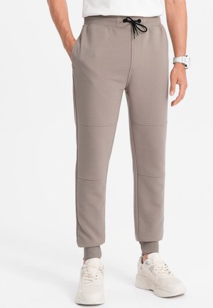 Pantalon de survêtement en polaire de couleur brun clair avec une finition texturée, ceinture élastique, cordon de serrage et finitions côtelées ; il comprend des poches latérales.