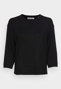 Sudadera negra, ligera, con cuello redondo y mangas de tres cuartos. Tiene un dobladillo acanalado y está hecha de una tela suave y texturizada.
