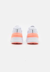 Zapatillas deportivas blancas con un upper texturizado, acentos rosas en el talón y una suela acolchada. Detalles reflectantes en la parte trasera.