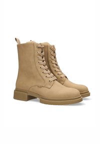 Stivali alla caviglia in pelle beige con una suola robusta e texturizzata. Presentano lacci, una morbida fodera e un manico sul retro per facilitare l'indossamento.