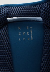 Tessuto blu con una sovrapposizione di rete testurizzata. Il testo dice "RECYCLED INSIDE" in lettere grigio chiaro. Fodera interna liscia visibile.