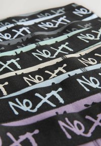 Schwarzer Stoff mit horizontalen Streifen in Pastellfarben, der das Wort "Next" in einer handschriftlichen Schriftart zeigt. Weiche Textur, unterschiedliche Streifenbreiten.