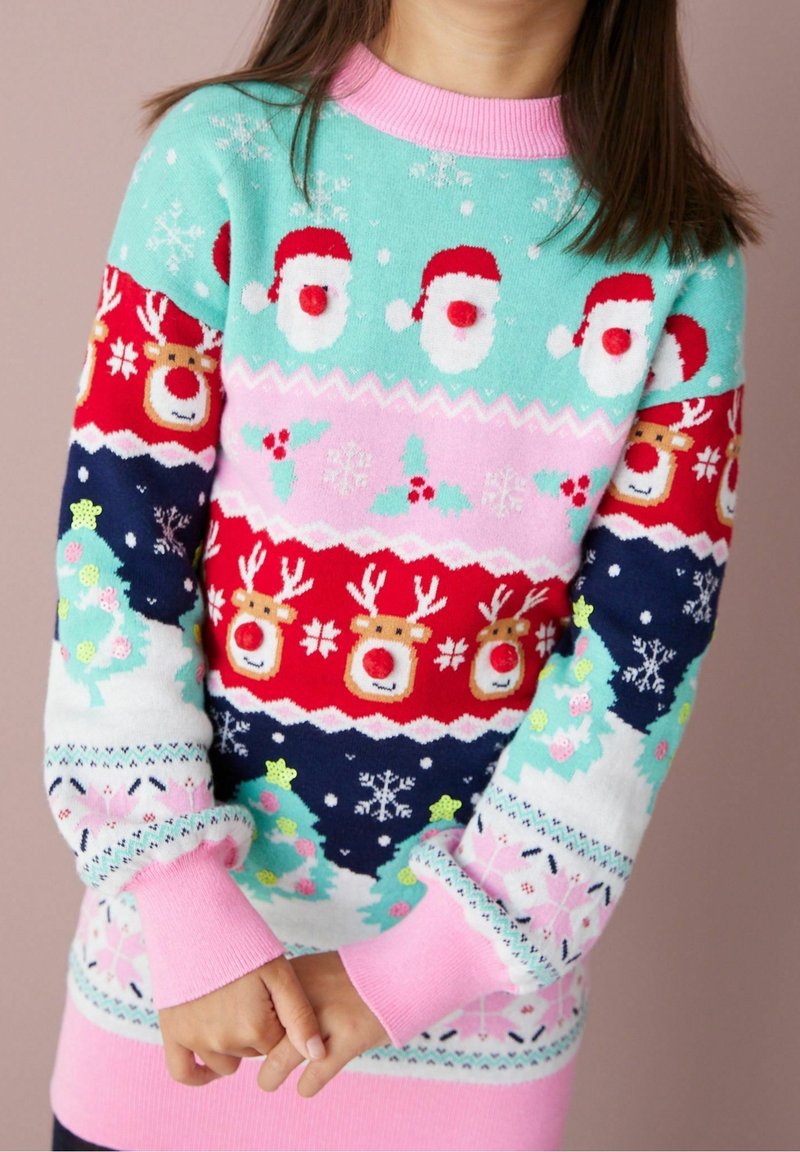 Enfant portant un pull de Noël coloré avec des visages du Père Noël, des rennes, des flocons de neige, du houx et des arbres décorés en rouge, rose, bleu et vert.