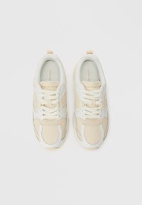 Zεύγος μπεζ και λευκών αθλητικών παπουτσιών Tommy Hilfiger με λευκές κορδόνες, σε θέα από πάνω σε λευκό φόντο.