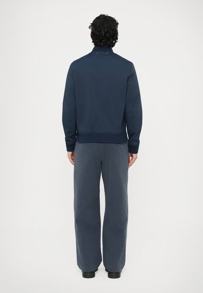 Námornícka bavlnená mikina s vysokým golierom, zakončená elastickými manžetami a lemom. Kombinovaná so sivými širokými textúrovanými nohavicami.