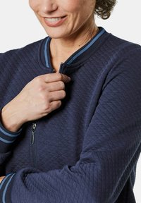 Marine blauwe gewatteerde jas met een ritssluiting, geribde kraag en gestreepte manchetten. De stof lijkt textuur te hebben en heeft een aansluitend ontwerp.