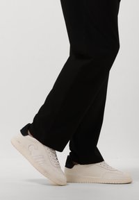 Witte leren sneakers met marineblauwe hakaccenten, ronde neus, gestructureerde zijkanten en vlakke rubberen zool, in combinatie met zwarte broek.