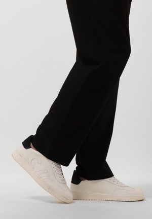 Witte leren sneakers met marineblauwe hakaccenten, ronde neus, gestructureerde zijkanten en vlakke rubberen zool, in combinatie met zwarte broek.