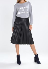 Gray long-sleeve sweatshirt with white text, paired with a black pleated midi skirt made of a shiny material, and navy ankle boots.