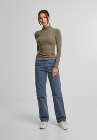 Długi rękaw, oliwkowa bluzka z golfem dobrana do jasnoniebieskich spodni typu straight leg i białych tenisówek z teksturowaną podeszwą.