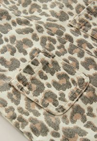 Læderprint stof med en beige bund og mørkebrune samt lysebrune pletter. Teksturen er blød, med synlige sømme og en lomme detalje.