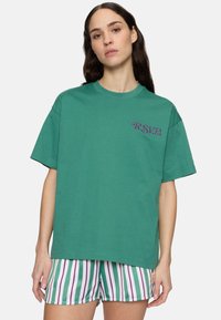Grøn bomulds T-shirt med korte ærmer og rund halsudskæring, med lilla "R.S.V.P." tekst på venstre side. Stribede shorts ses nedefra.