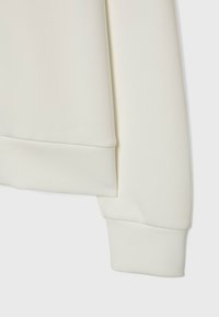 Bílá světlovka s hladkou texturou, s žebrovaným manžetou na konci rukávu. Jednoduchý, minimalistický design bez vzorů či akcentů.