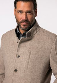 Abrigo de mezcla de lana beige con cuello alto, cierre de botones y bolsillo lateral. Tejido texturizado con un patrón de espiga y acentos marrones.