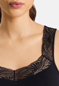 Top senza maniche nero con un delicato bordo in pizzo attorno al colletto, con un motivo ondulato e una texture liscia. Vista ravvicinata dei dettagli del tessuto.