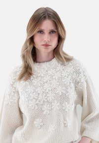 Chunky cremefarbener Strickpullover mit strukturieller Blumenstickerei, geripptem Rundhalsausschnitt und locker sitzenden Ärmeln.