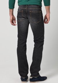 Tmavě denimové džíny s přímým střihem, zdobené oranžovým šitím, se dvěma zadními kapsami a hladkou texturou. Nosit je s námořnicky modrými botami.