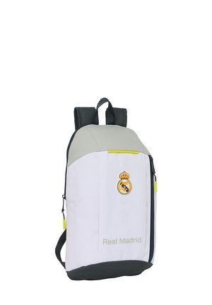 Sac à dos blanc avec des accents gris, présentant un logo du Real Madrid, une tirette de fermeture éclair jaune et des bretelles réglables. Design vertical avec une texture lisse.