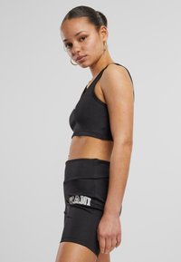 Čierny crop top a sukňový set vyrobený z elastického materiálu, s priliehavým strihom a logom na sukni. Hladká textúra, minimalistický vzhľad.