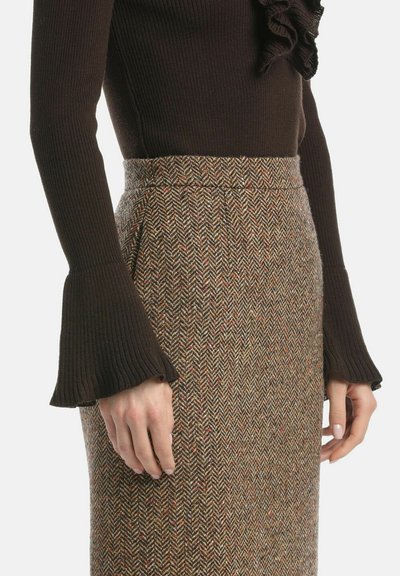 Brązowy sweter z prążkowaną strukturą i rozszerzanymi mankietami, w połączeniu z wełnianą spódnicą w wzór houndstooth w ziemistych odcieniach i subtelnymi kolorowymi akcentami.