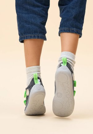 Schuhe für Kinder mit einem grauen Textilobermaterial, grünen Akzenten und einer strukturierten grauen Gummisohle. Verstellbare Riemen und weiche graue Socken sind sichtbar.