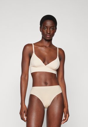 Beige bralette dengan desain silang dan tali tipis, dipadukan dengan celana dalam tinggi yang serasi, terbuat dari kain lembut dan elastis.
