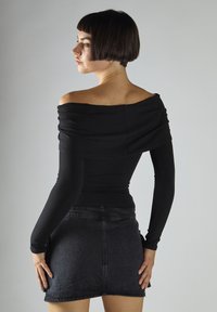 Top nero scollato sulle spalle con maniche lunghe, tessuto a coste e design aderente, abbinato a una mini gonna in denim scuro. Look semplice e pulito.