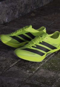 Bright yellow athletic shoes with black stripes, lightweight material, textured upper, closely spaced laces, and a pointed toe design.
