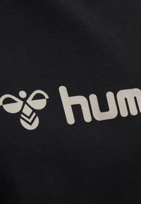 Tela negra con un logo blanco que incluye una ilustración de una abeja y la palabra "hum" en una tipografía moderna, superficie texturada con un ligero brillo.