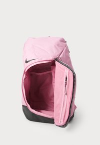 Rožaina Nike mugursoma ar galveno nodalījumu, acu kabatu un melnu apakšu. Iekļauj rāvējslēdzēja aizdares un gludu, izturīgu audumu.