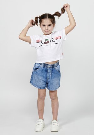 T-shirt blanche raccourcie avec un graphique "LOVE" et une cerise, associée à un short en denim bleu clair avec taille élastique et deux poches avant. Baskets blanches.