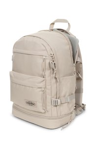 Zaino beige con scomparto imbottito per laptop, molteplici tasche, spallacci regolabili e base rinforzata per una maggiore durabilità. Caratterizzato dal logo del marchio.