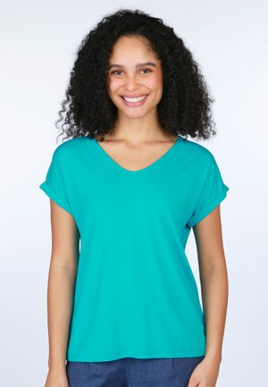Türkisfarbenes V-Ausschnitt-T-Shirt mit umgeschlagenen kurzen Ärmeln, aus weichem Stoff gefertigt. Hat eine lockere Passform und eine glatte Textur. Wird über dunklen Hosen getragen.