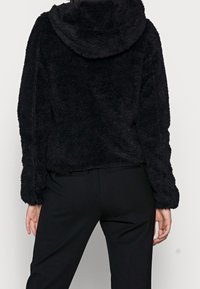 Felpa nera in tessuto morbido e peloso. Presenta un grande cappuccio e maniche ampie, con una lunghezza cropped, abbinata a pantaloni neri.