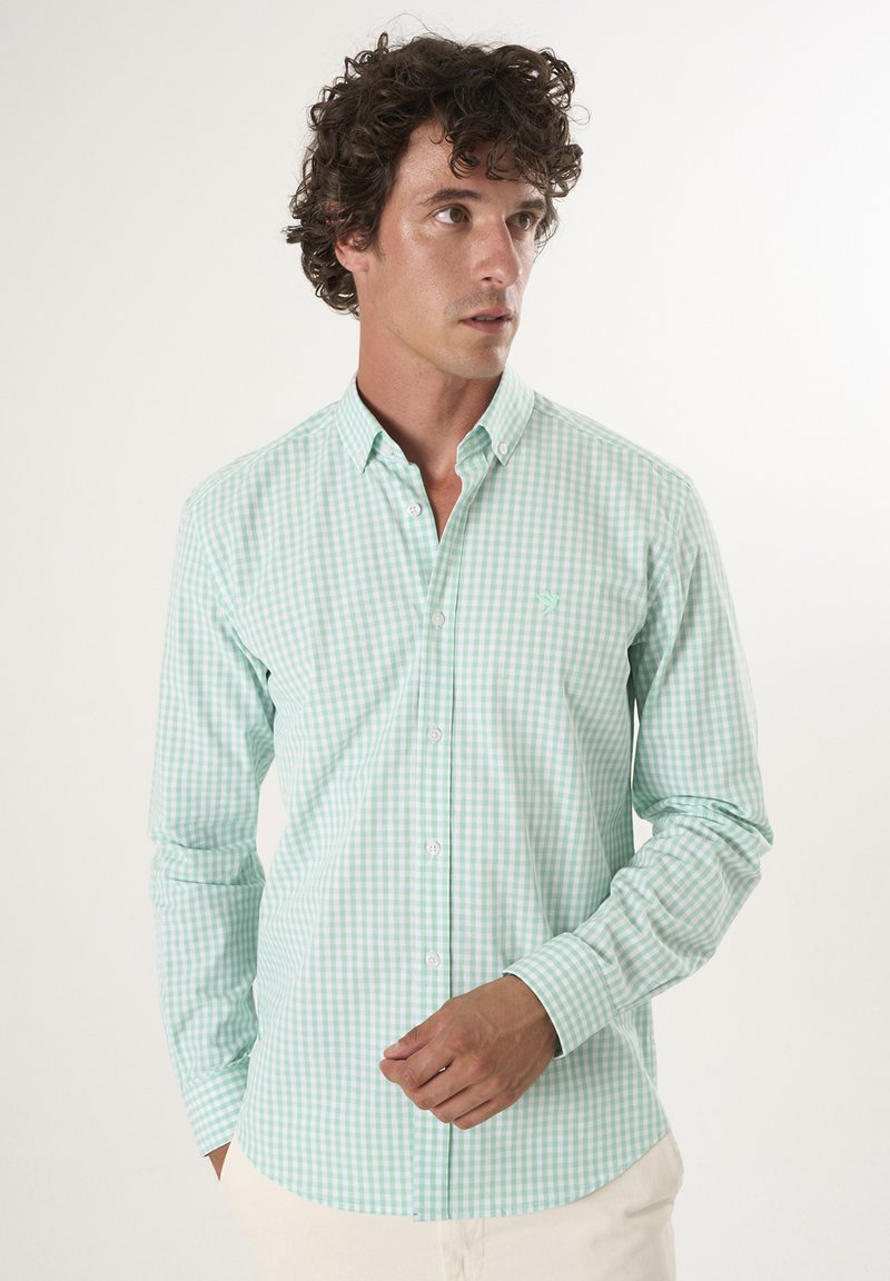 Camisa de cuadros en verde menta con botones y mangas largas, cuello puntiagudo y un pequeño logo en el lado izquierdo del pecho. Tejido de algodón suave.