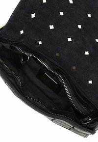 Borsa a tracolla in suede nera con borchie quadrate bianche all'esterno e chiusura con zip. Interno foderato in tessuto nero e etichette del marchio.