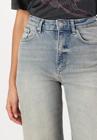 Lichtblauwe denim jeans met een hoge taille, vervaagde textuur, vijf zakken en een knoopsluiting; lichte slijtage nabij de tailleband.
