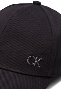 Casquette noire avec un design structuré, présentant une texture côtelée et un logo 'CK' en relief dans une finition métallique foncée.