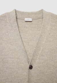 Helle beige Strickjacke mit V-Ausschnitt, ausgestattet mit einem dunkelbraunen Knopf vorne und einem weichen, strukturierten Stoff. Markenetikett sichtbar.