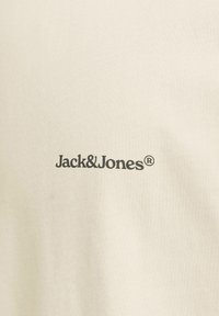Bežinis medvilninis marškinėliai su juodu "Jack & Jones" logotipu spausdintu per krūtinę. Sklandus paviršius su apvaliu iškirpimu.