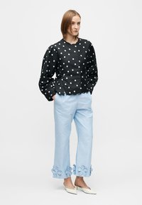 Juodas juodų taškelių palaidinė su pūstomis rankovėmis ir apvalia iškirpte, derinama su šviesiai mėlynomis kelnėmis su gėlių aplikacijomis krašte. Baltos smailios kojinės.