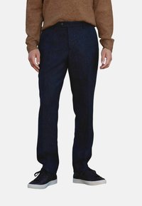 Marineblauwe wollen broek met een rechte pasvorm, voorzien van een platte voorkant, riemlussen en zijzakken, gecombineerd met zwarte schoenen en een bruine trui.